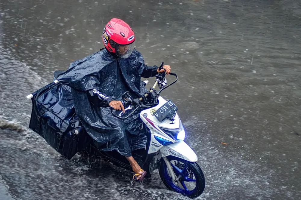 a-package-courier-who-rides-a-motorbike-who-drives-through-flood-waters-during-heavy-rain-in-a-residential-area-indonesia-8-december-2023-free-photo